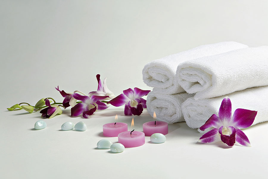 Spa in Faisalabad offering a luxurious experience with rolled white towels, scented candles, and fresh orchids for ultimate relaxation.